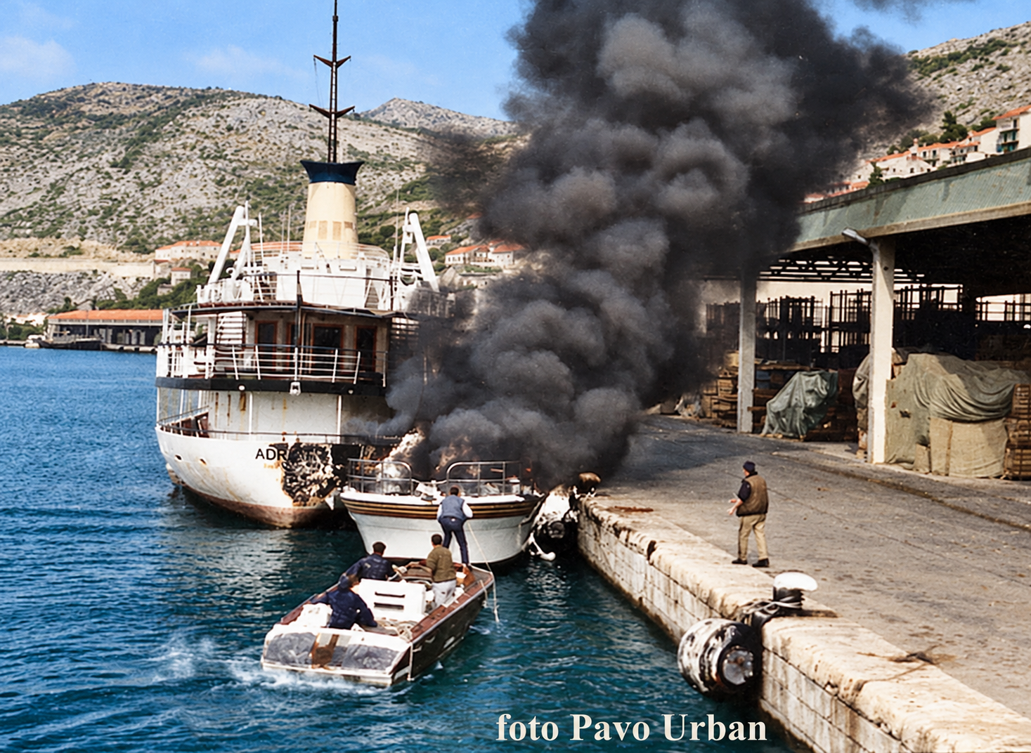 Adriatic u požaru u Gružu tijekom ratnog stradanja 1991. Kolorizirana verzija izvorne crno-bijele fotografije Pava Urbana. Boje su naknadna rekonstrukcija.