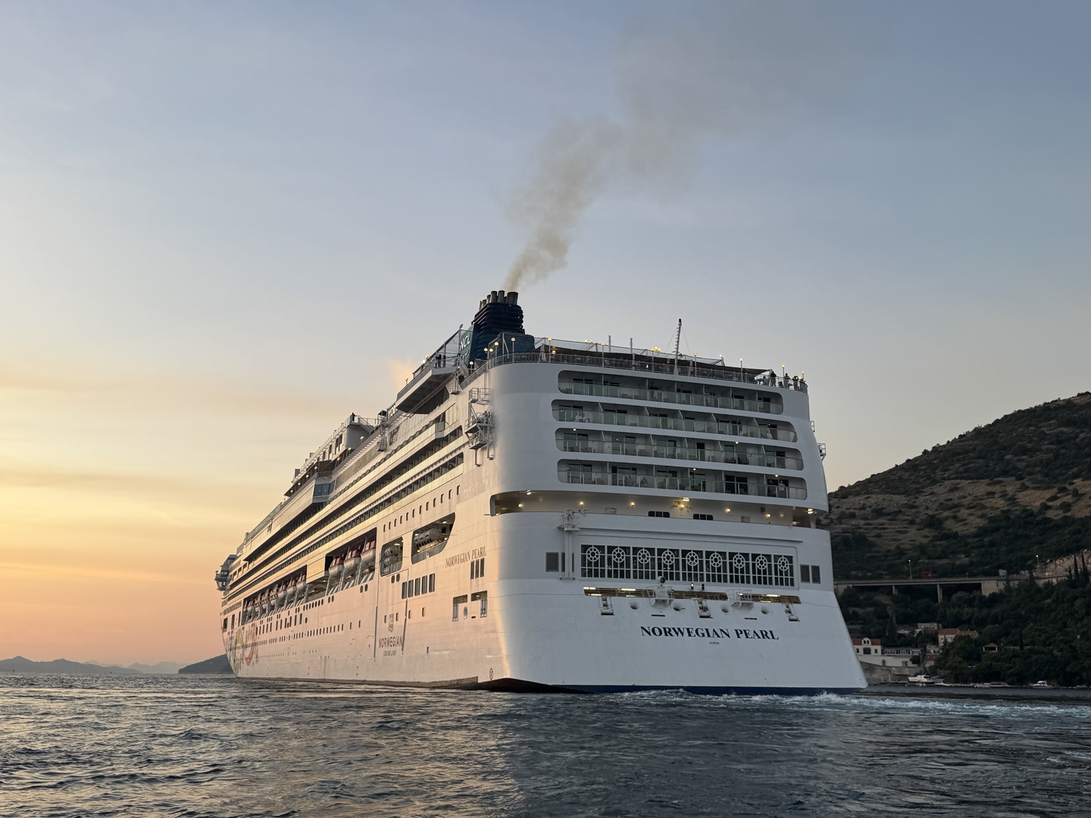 Norwegian Pearl u akvatoriju Gruža pri zalasku sunca; bočni pogled s krme i obala u pozadini. Izvorna datoteka IMG_2881.jpeg.